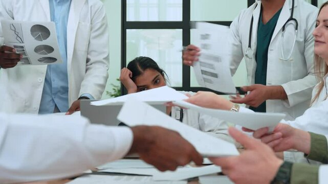 Healthcare professionals experiencing intense workplace stress, throwing medical documents during heated meeting, revealing underlying tension and burnout among diverse medical team - Powered by Adobe