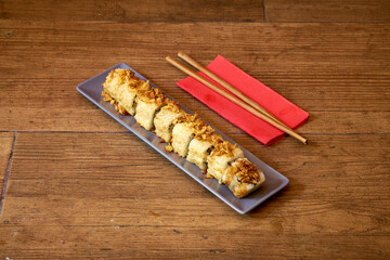 A plate of food with chopsticks on a red napkin. The food is a roll with a topping