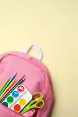 A pink backpack with colorful school supplies on a pastel backdrop