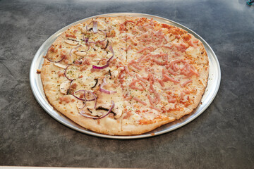 A pizza with onions and ham on it. The pizza is cut into four pieces. The pizza is on a metal pan