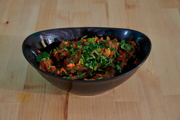 A bowl of food with a green herb on top. The bowl is black and sits on a wooden table