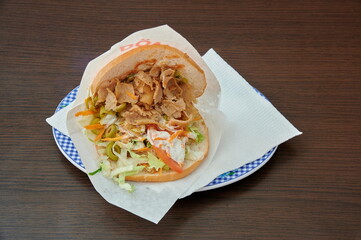 A sandwich with meat and vegetables on a plate. The plate is on a table. The sandwich is covered with a napkin