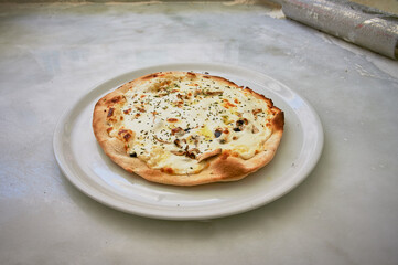 A pizza is sitting on a white plate. The crust is brown and the cheese is melted. There are some herbs sprinkled on top of the pizza