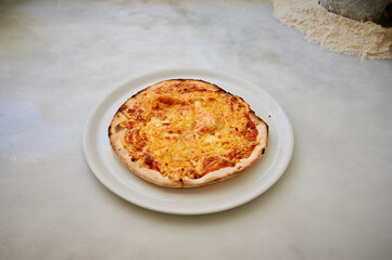 A pizza is sitting on a white plate. The crust is thin and the cheese is melted. The pizza is placed on a table