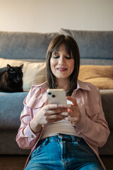 Woman using smartphone at home with black cat relaxing on sofa