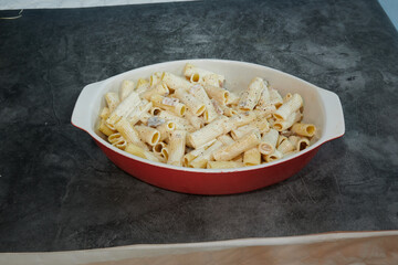 A red bowl of pasta with a white sauce. The pasta is in the shape of a tube