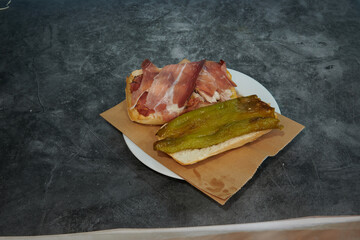 A sandwich with ham and peppers sits on a plate. The plate is on a counter. The sandwich is cut in half