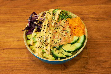 A bowl of food with avocado, cucumber, and carrots. The bowl is blue and has a creamy sauce on top