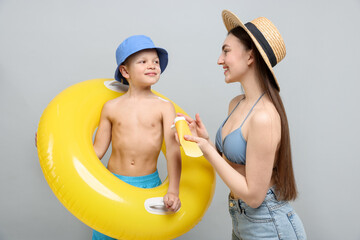 Mother with sun protection cream and her son on light grey background