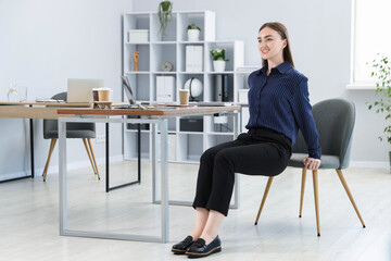 Beautiful woman exercising with chair in office