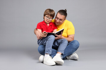 Father and his son reading book together on grey background