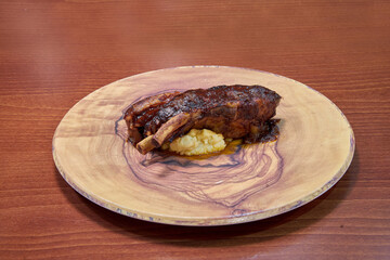 A plate of meat with mashed potatoes on top. The plate is wooden and the meat is brown