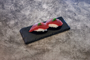 A plate of sushi with a black plate underneath it. The sushi is red and white. There is a green garnish on top of the sushi