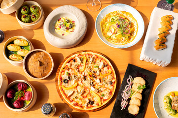 Top view of assorted food items on a brown table including mushroom dim sum, prawn and veg dumplings, wild salmon nigiri, chicken spiced pizza, cheese nuggets, veg salad and gulab jamun with rabri.