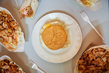 A plate with a hamburger sits on a table with other plates of food. There are forks and knives on the table as well