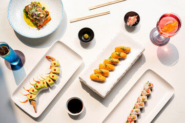 Top view of tempura rolls, wild salmon nigiri, and dragon roll sushi in white trays with soy sauce,...