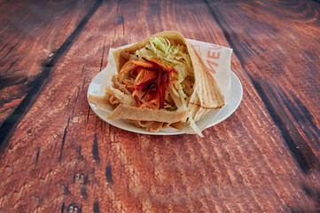 A wrap with meat and vegetables on a plate. The wrap is on a wooden table