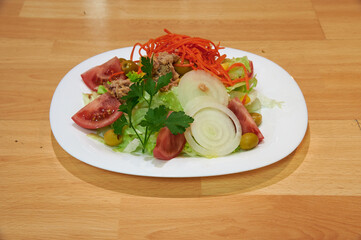 A salad with tomatoes, carrots, and onions on a white plate. The plate is on a wooden table