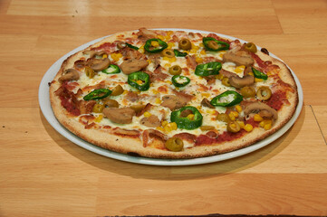 A pizza with mushrooms, peppers, and olives on a white plate. The pizza is on a wooden table