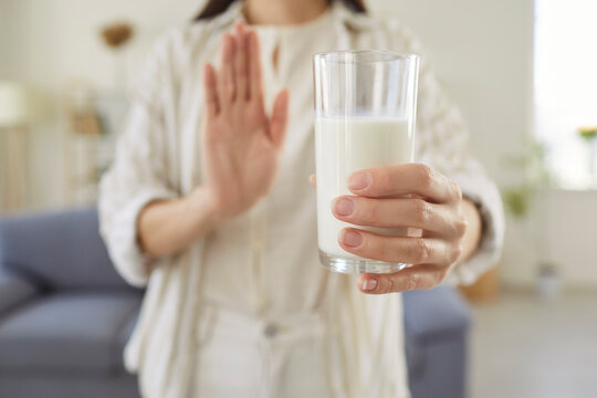 Close up of young woman holding glass of milk and showing refusal gesture with hand. Female person rejecting dairy product due to lactose intolerance, allergy, dietary choice or health concern.