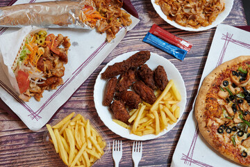 A table with a variety of food including chicken wings, french fries, and pizza. There are also some condiments and utensils on the table
