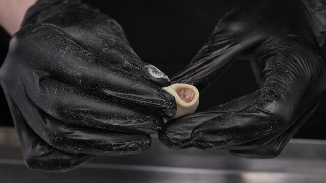 Close-up of hands in latex gloves making dumplings stuffed with meat.