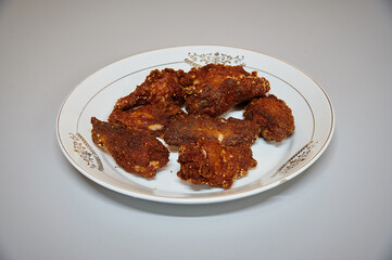 A plate of fried chicken with a white plate. The chicken is golden brown and has a lot of seasoning