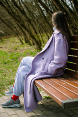 Woman Sitting and Relaxing on a Bench in a Purple Coat
