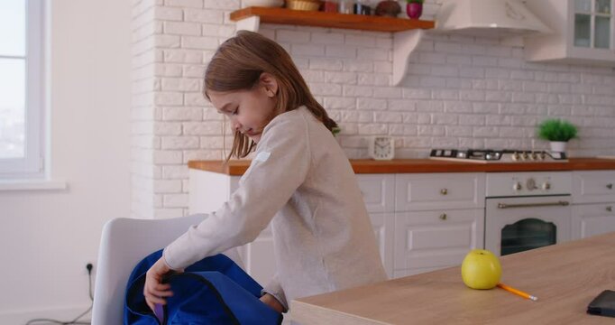Portrait of little schoolboy preparing his schoolbag for school lessons putting textbooks. Child boy packing backpack at home. Back to school, knowledge and education concept. 4k video.