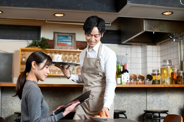 飲食店で女性客に食事の配膳をする男性店員