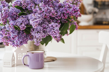 A large purple bouquet of lilacs, white Scandinavian houses and a cup of tea on the table. In the...