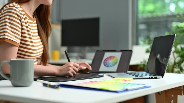 Young female designer using pen tablet and color palette while working in a modern creative office and color theory themes.