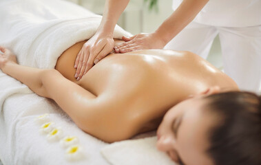 Close up of masseur performing back massage to relaxed young woman lying on massage table in spa...