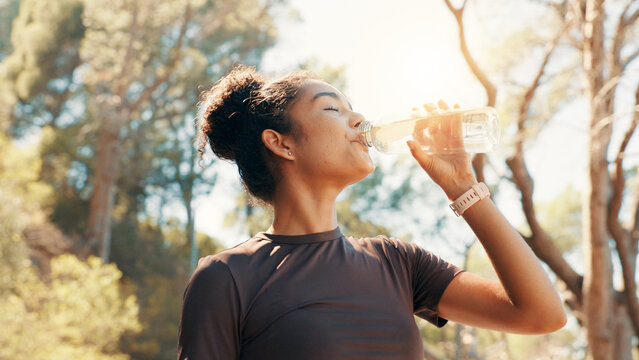 Woman, drinking water and fitness in nature for hydration, electrolytes and body detox. Low angle, runner and thirsty in forest with H2O, exercise break and liquid for gut health with digestion aid