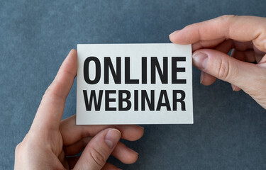 White card in hands with the inscription Online Webinar on a gray background