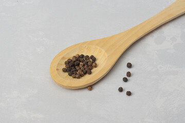 Black peppercorns on a wooden spoon and on a gray background. Dry spicy seasoning for ready meals. Flat lay