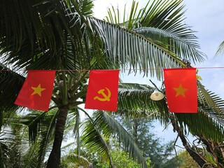 Vietnamese national flags hang between coconut palms at a tropical resort in Binh Thuan, Vietnam.