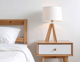 Light wood bedside table with modern lamp against minimalist white wall. Scandinavian bedroom with neatly made bed and neutral tones.