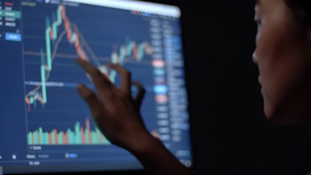 Individual analyzes stock trading charts on a computer screen in a dark environment. The focus is on insightful market trends and investment strategies.