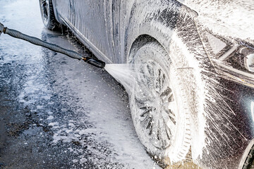 Driver washing car with contactless high pressure water jet,equipment pump in self service car wash.Vehicle covered with foam chemical detergents