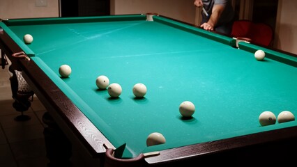 Playing Russian billiards on a green table. A beginner player hits a white ball with a cue at another unsuccessfully. A failure shot. Practicing in sport game. Pastime at home game hobby