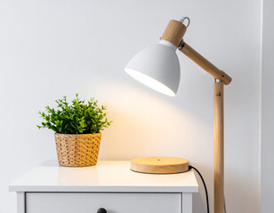 White nightstand with wooden table lamp and green potted plant against neutral background. Modern bedroom detail