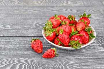 in a white plate large ripe strawberries on a gray wooden background