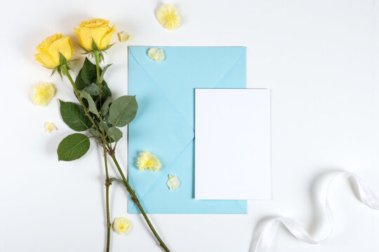 yellow roses and a blue envelope on a white table