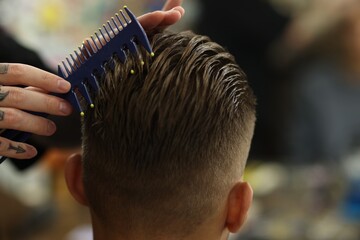 Professional barber making stylish haircut in barbershop, closeup