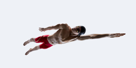 Obraz premium Focused male swimmer in red shorts, goggles and cap extending arm in freestyle pose, muscles tensed in suspended motion against white backdrop. Concept of sport, training, discipline, motion