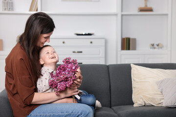 Mother and her son with bouquet of lilac flowers at home, space for text