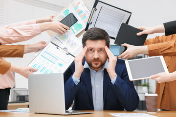 Man overwhelmed by different requests from colleagues at desk in office