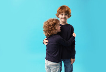 Cute little brothers hugging on light blue background. Space for text