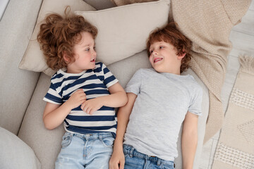 Cute little brothers laying together on sofa, above view